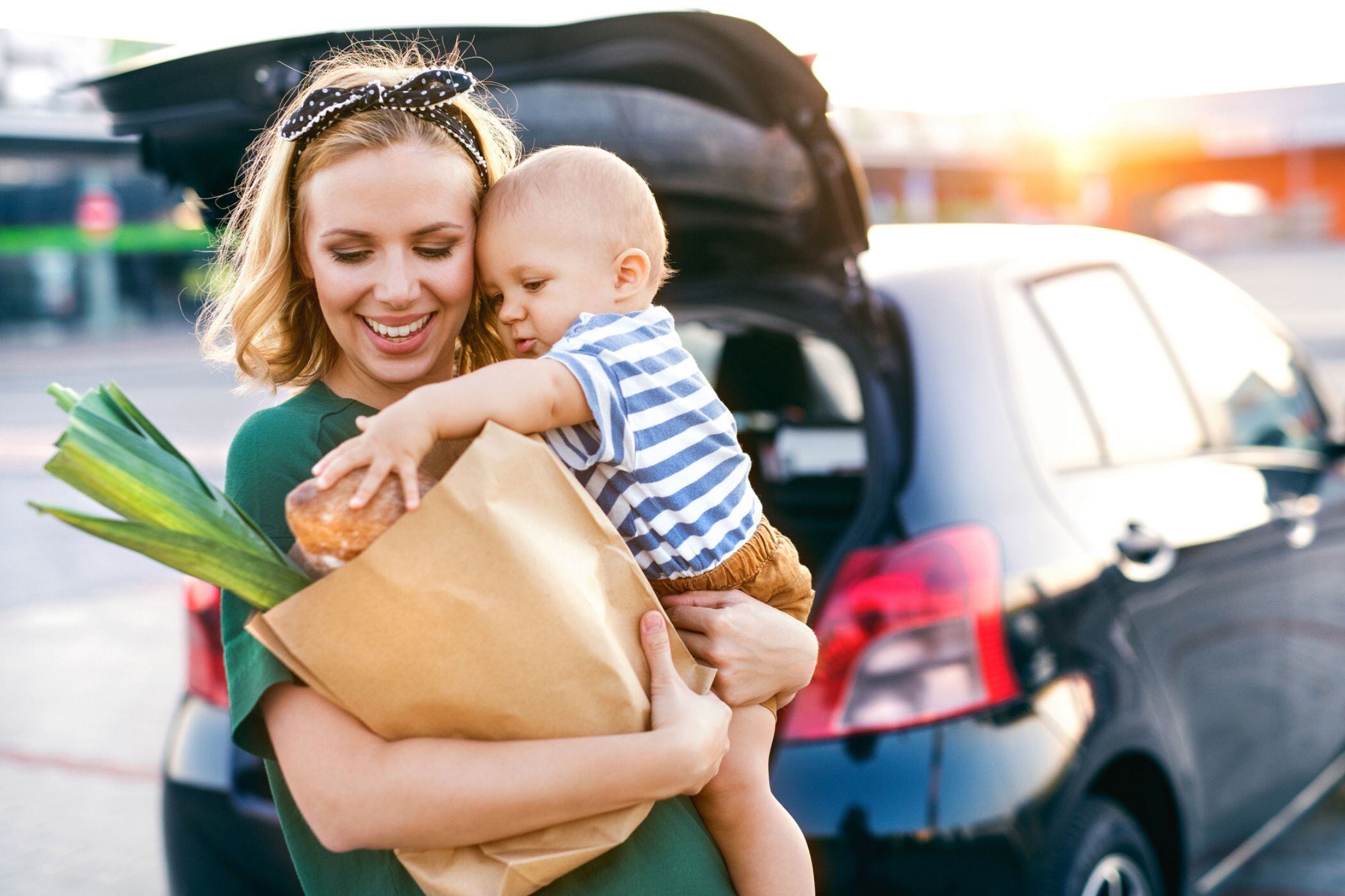woman in grocery store parking lot holding baby and bag of gifted groceries